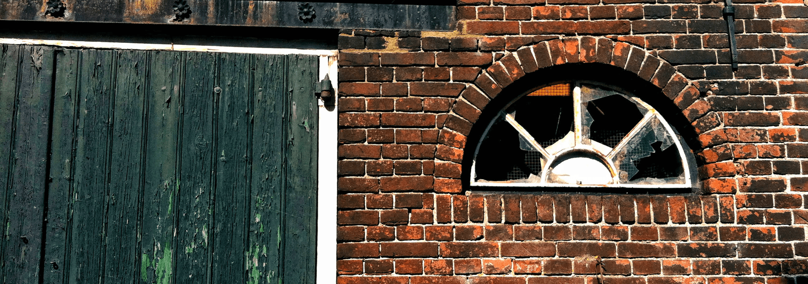 Weathered green timber doors beside a broken arched window