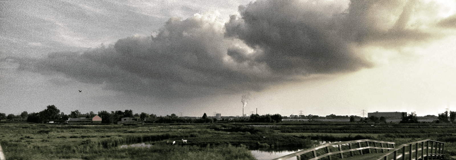 Storm clouds advancing over fields and an industrial horizon